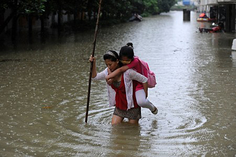 7月5日，安徽省一名女子背著她的女兒穿過淹水區。（STR/AFP/Getty Images)