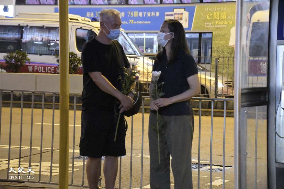 兩位被機動部隊截查的市民手持白色菊花。（麥碧/大紀元）