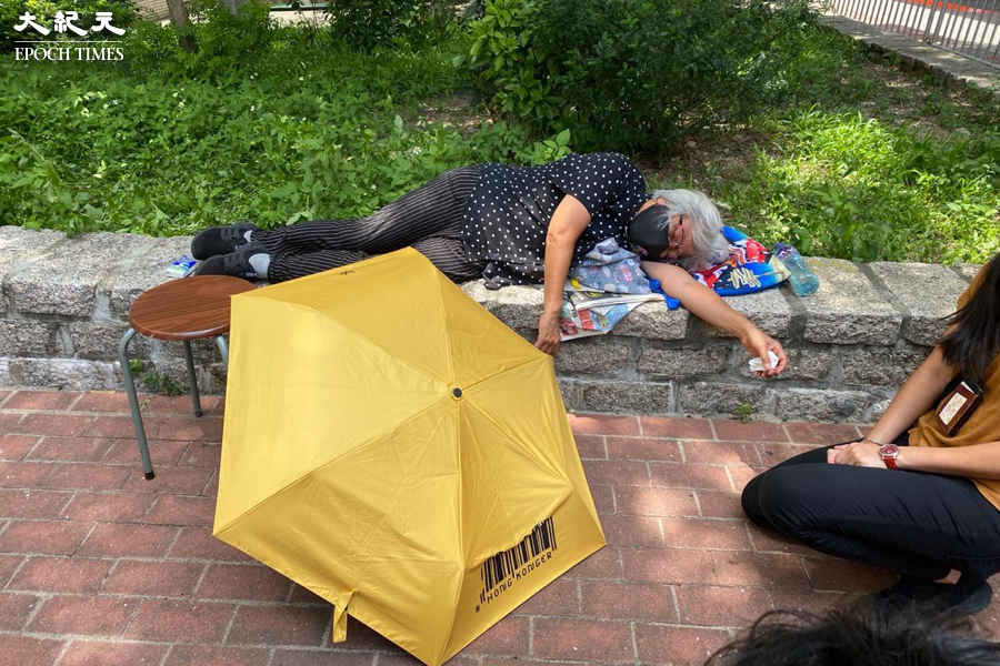 她被警員抬到法院範圍外隨後感到不適，躺倒在法院外石台上。（梁珍／大紀元）