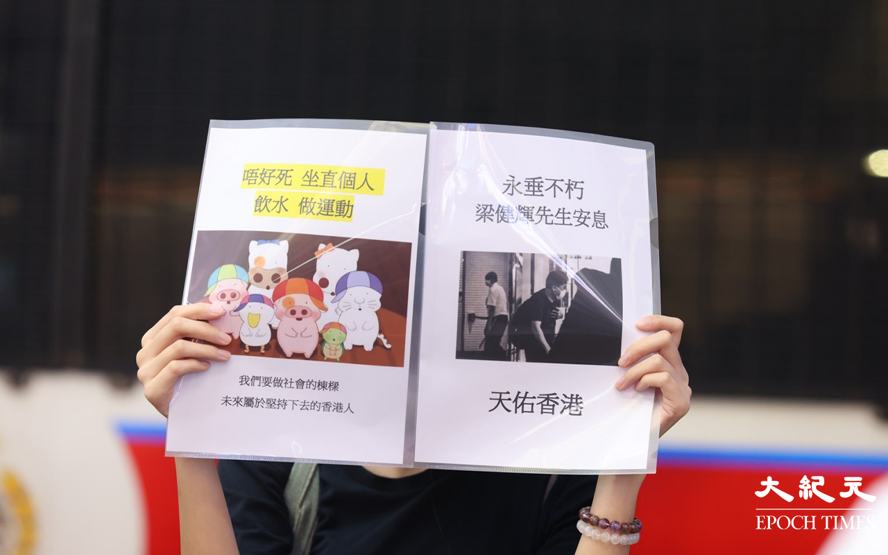 約七時三十分，有女子在SOGO百貨對出馬路旁舉高一張寫有「永垂不朽，梁健輝先生安息，天佑香港。」隨後警員見狀立即上前圍封該女子及截查她身份。（李辰／大紀元）