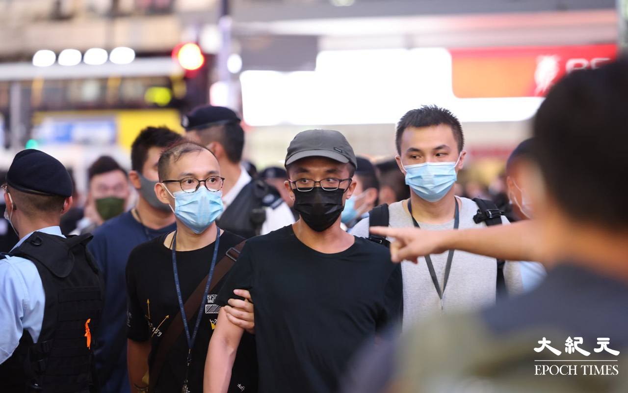 約七時三十分，有女子在Sogo對出馬路旁舉高一張寫有「永垂不朽，梁健輝先生安息，天佑香港。」隨後警員見狀立即上前圍封該女子及截查她身份。亦有兩名男子被截查後帶走上警車離開，未知拘捕原因。（李辰／大紀元）