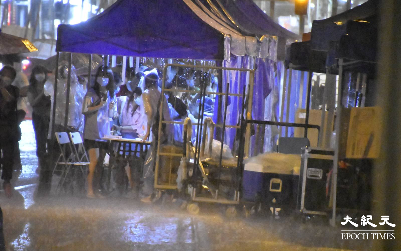 晚上10時30分，現場突然落起大雨，正進行檢測的市民，顯得有點狼狽。（李辰 / 大紀元）