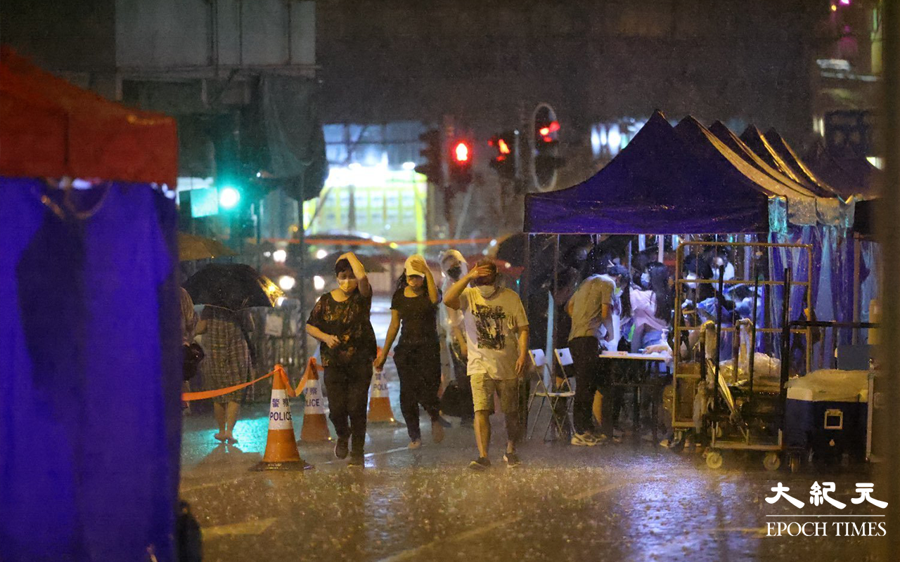 晚上10時30分，現場突然落起大雨，正進行檢測的市民，顯得有點狼狽。（麥碧 / 大紀元）