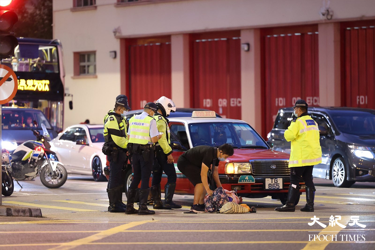 涉事的士撞到老婦人後，將老婦人的手拉車等雜物件進車底，黑衣者為老婦人家屬。（李辰／大紀元）