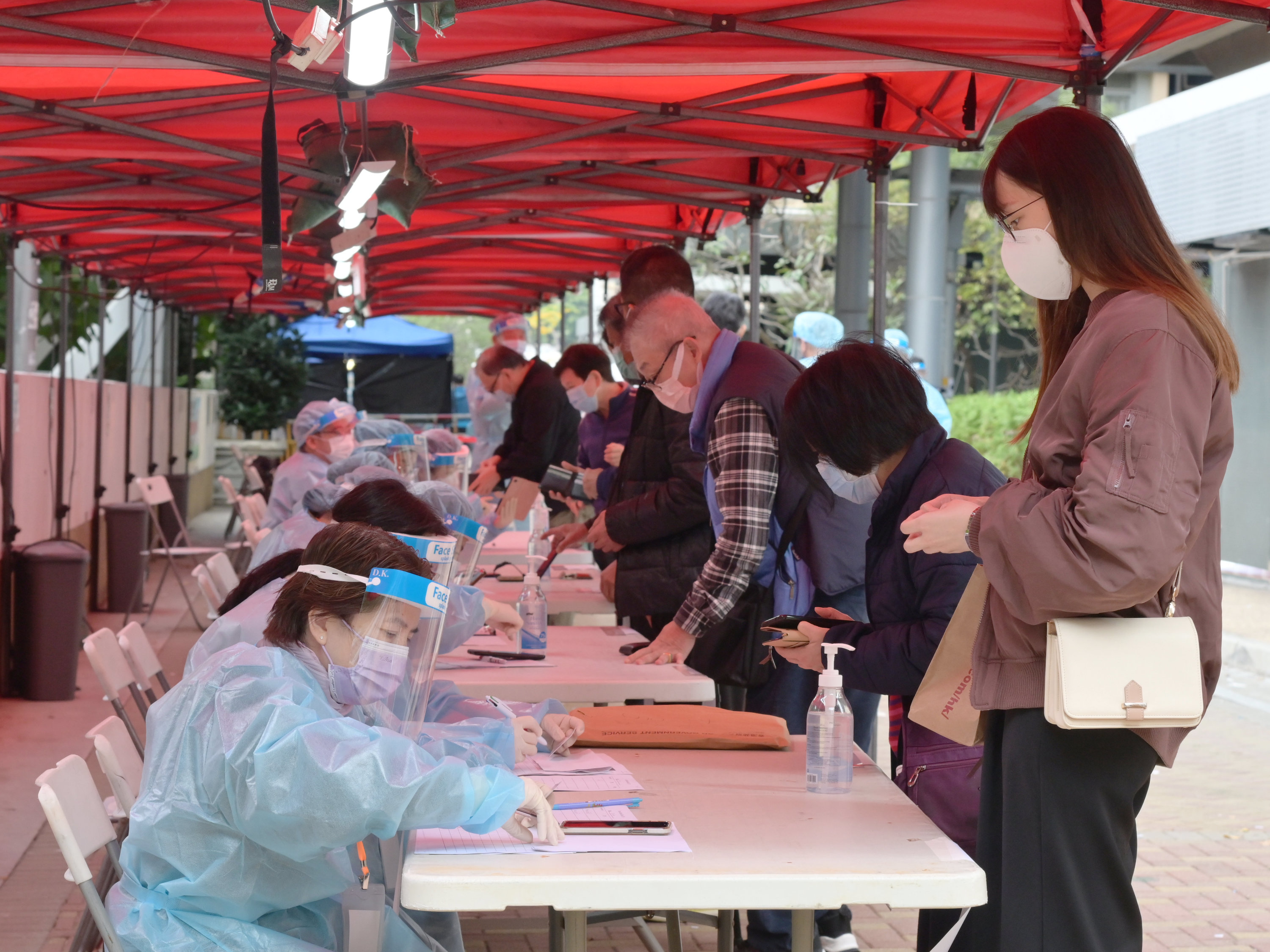政府昨日（22日）就葵涌指明「受限區域」（即葵涌邨曉葵樓）作出限制與檢測宣告及強制檢測公告，限制在葵涌指明「受限區域」內的人士須留在其處所並接受強制檢測。圖示工作人員在「受限區域」內進行執法行動，檢查受限人士是否已接受強制檢測。（政府新聞處）