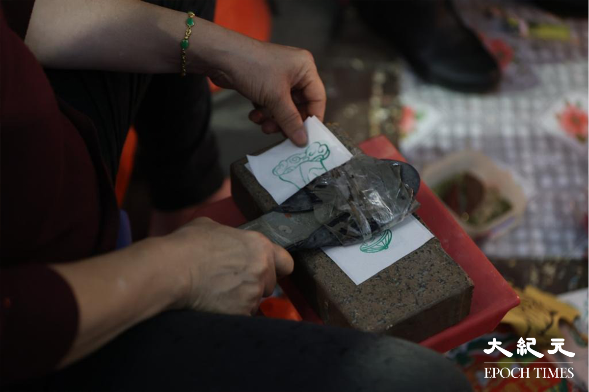 驚蟄打小人時，小人婆(負責打小人的婆婆)一般會用膠拖鞋，不斷打寫有小人名字的物品。攝於2021年3月5日。（胡凱欣／大紀元）