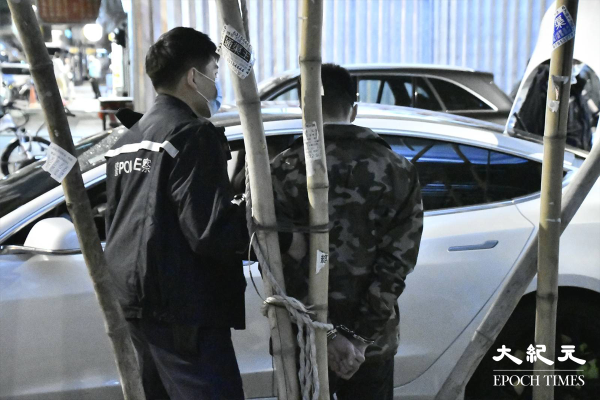警員將涉嫌販毒的20餘歲男司機（穿迷彩外套者）鎖上手銬，押在涉案Tesla私家車旁協助搜證。（麥碧／大紀元）