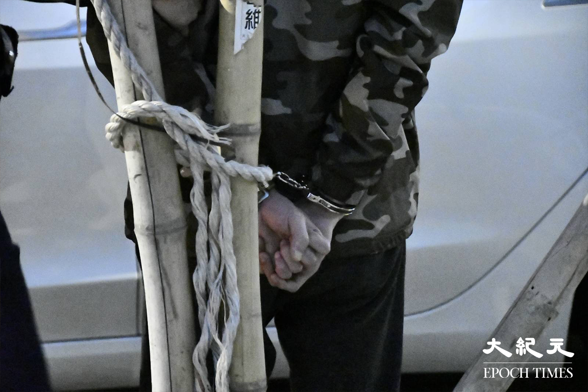 警員將涉嫌販毒的20餘歲男司機（穿迷彩外套者）鎖上手銬，押在涉案Tesla私家車旁協助搜證。（麥碧／大紀元）