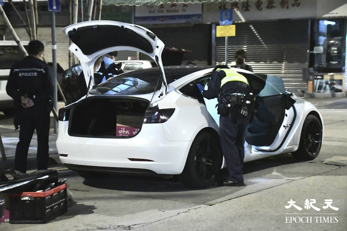 警員將涉嫌販毒的20餘歲男司機（穿迷彩外套者）鎖上手銬，押在涉案Tesla私家車旁協助搜證。（麥碧／大紀元）