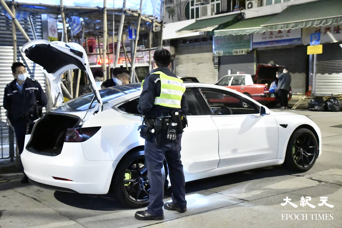 警員將涉嫌販毒的20餘歲男司機（穿迷彩外套者）鎖上手銬，押在涉案Tesla私家車旁協助搜證。（麥碧／大紀元）