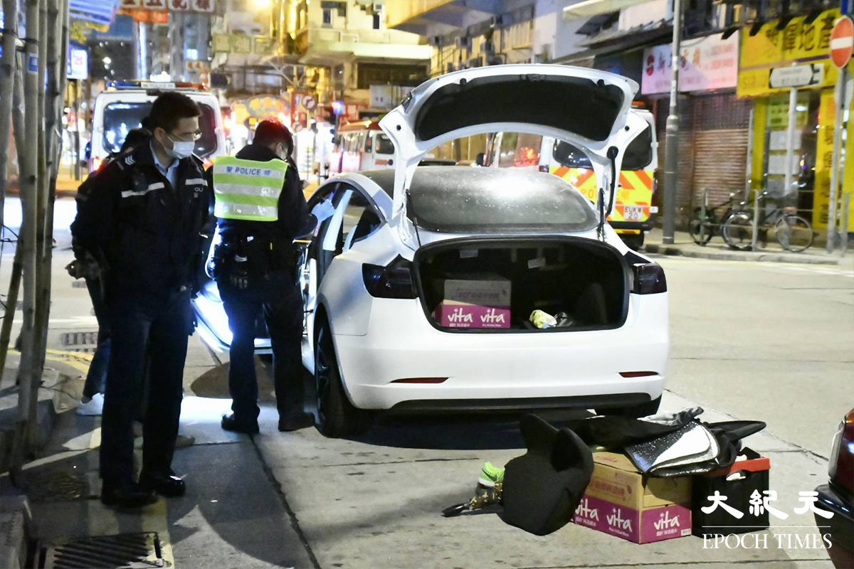 警員將涉嫌販毒的20餘歲男司機（穿迷彩外套者）鎖上手銬，押在涉案Tesla私家車旁協助搜證。（麥碧／大紀元）
