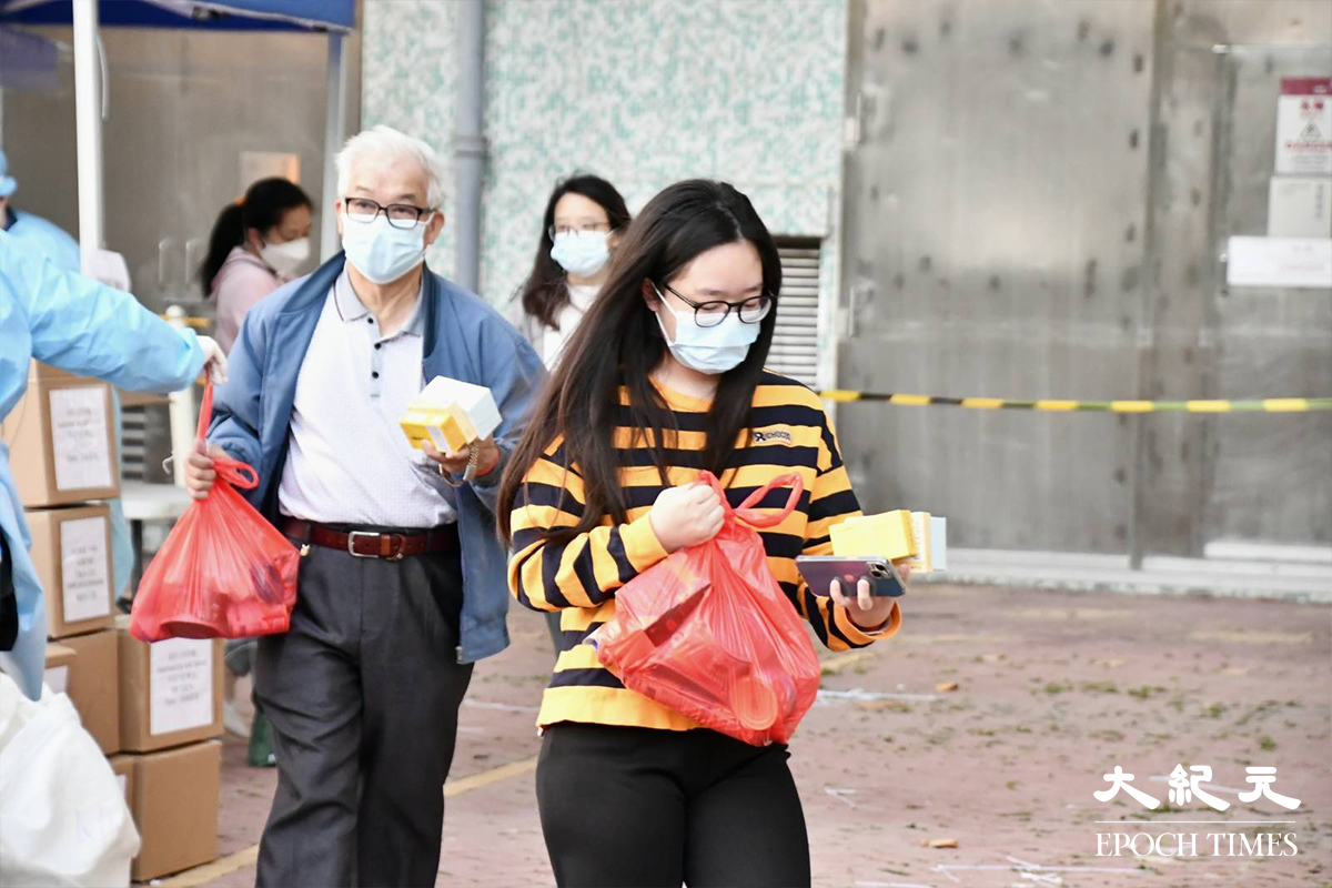 工作人員為完成強制檢測的住戶扣上手帶，並向他們派發物資包。（麥碧／大紀元）