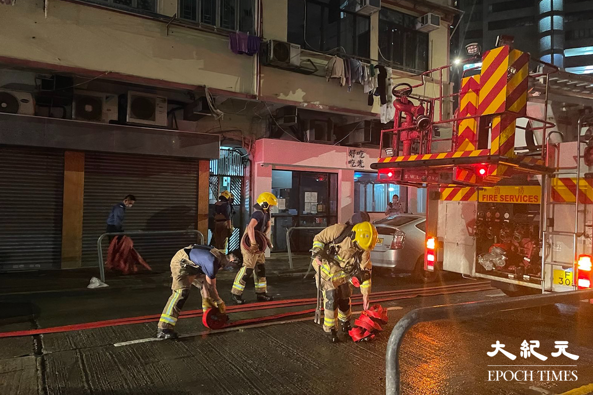 消防將火救熄後，於現場調查起火原因。警員向現場街坊了解事發經過。（卓相如／大紀元）