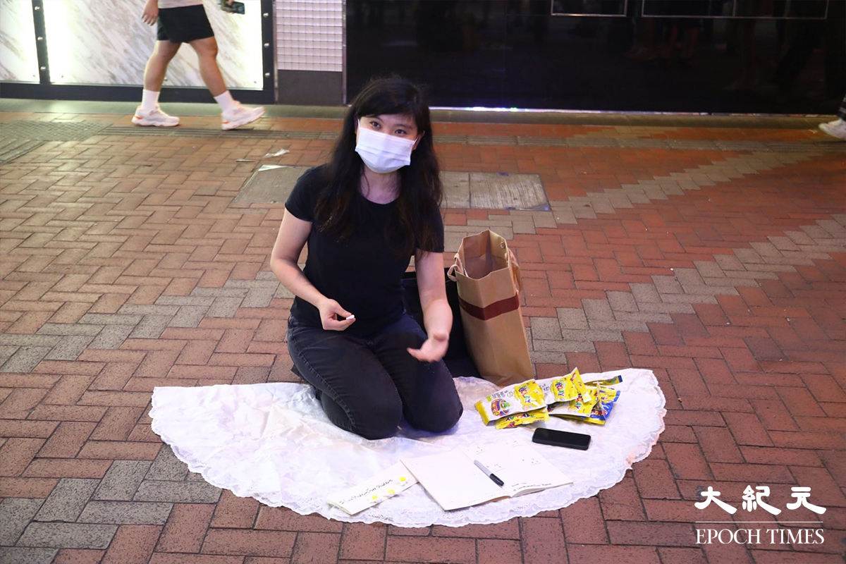 穿著黑色衣服的一位女行為藝術家，膝前放有簿和筆，讓路過途人回答簡單算術題。如答對了，她會向參與者送上一份小禮物。（胡琪／大紀元）