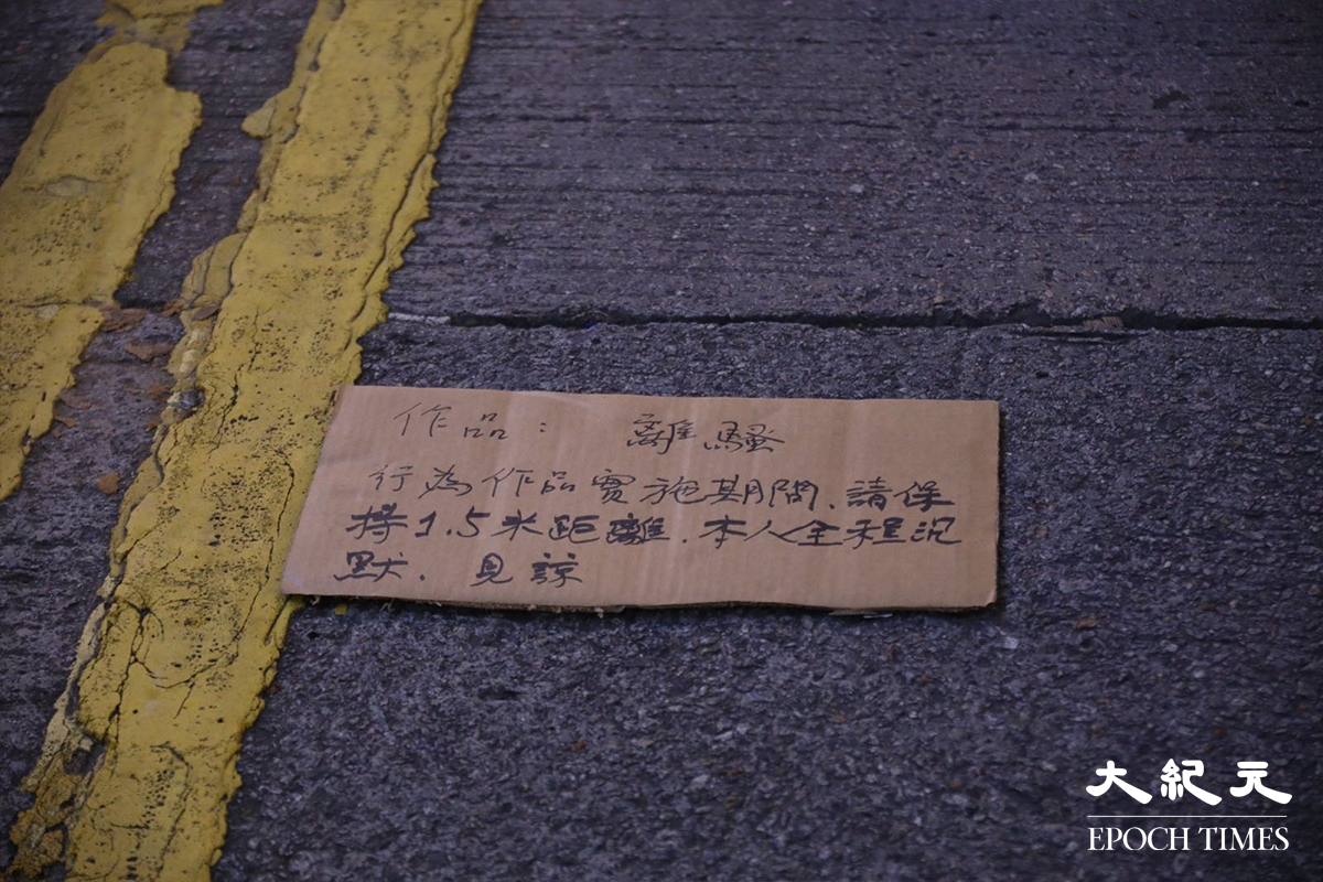穿著白色恤衫的男行為藝術家，在身旁放有卡紙提醒觀看市民，緊記保持適當社交距離。他以酒精，於地上的一卷白紙上，寫上「離、騷」二字。（胡琪／大紀元）