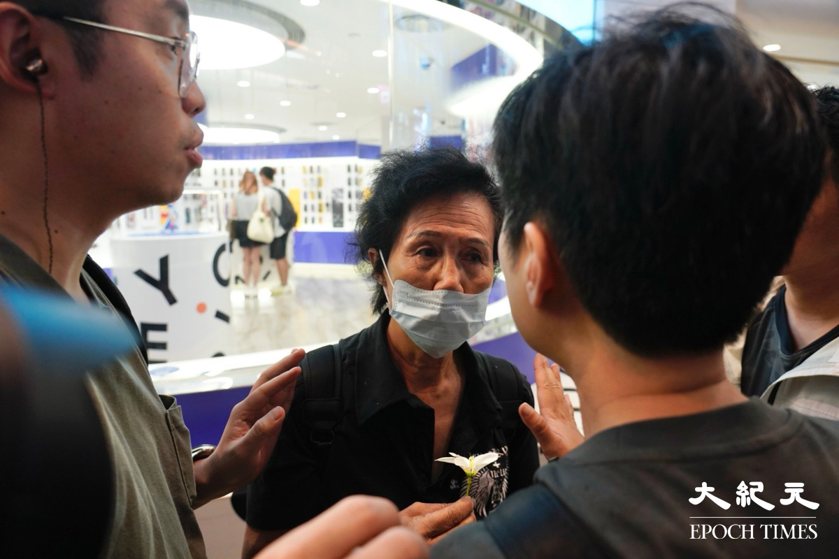 一名女士拿著一朵白色小花在銅鑼灣被截查，之後被警員「護送」入地鐵離開。（霄龍／大紀元）