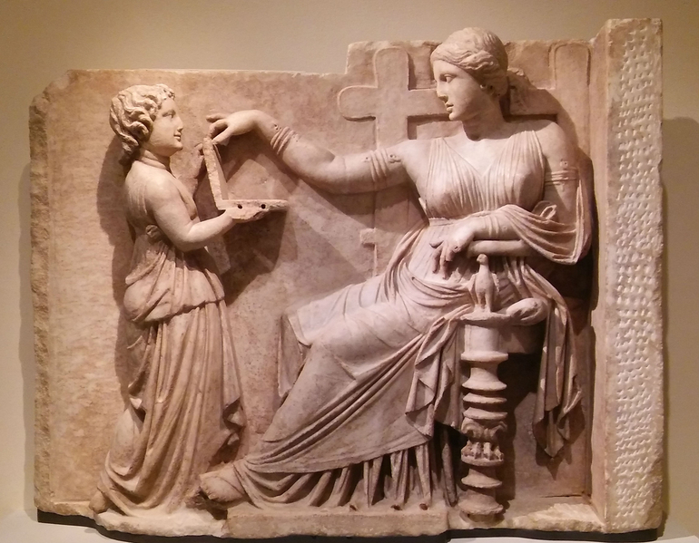 古希臘大理石墳墓浮雕：Grave Stele of an Enthroned Woman with an Attendant，約公元前100年的希臘化晚期，馬里布保羅‧蓋蒂博物館藏。作品文字說明上說：「女死者考究的服飾，華麗的高背椅和婢女舉到她面前的鏡子（或梳妝匣，留意那不是筆記本電腦），均可見出其社會地位很高。」(Kati Vereshaka/Epoch Times)