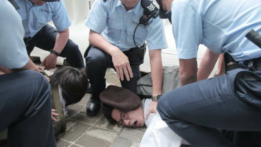 羅冠聰在示威現場舉起標語不到 5 秒即被十多名警察按在地上,造成手肘擦傷,狀甚痛苦。(潘在殊/大紀元)
